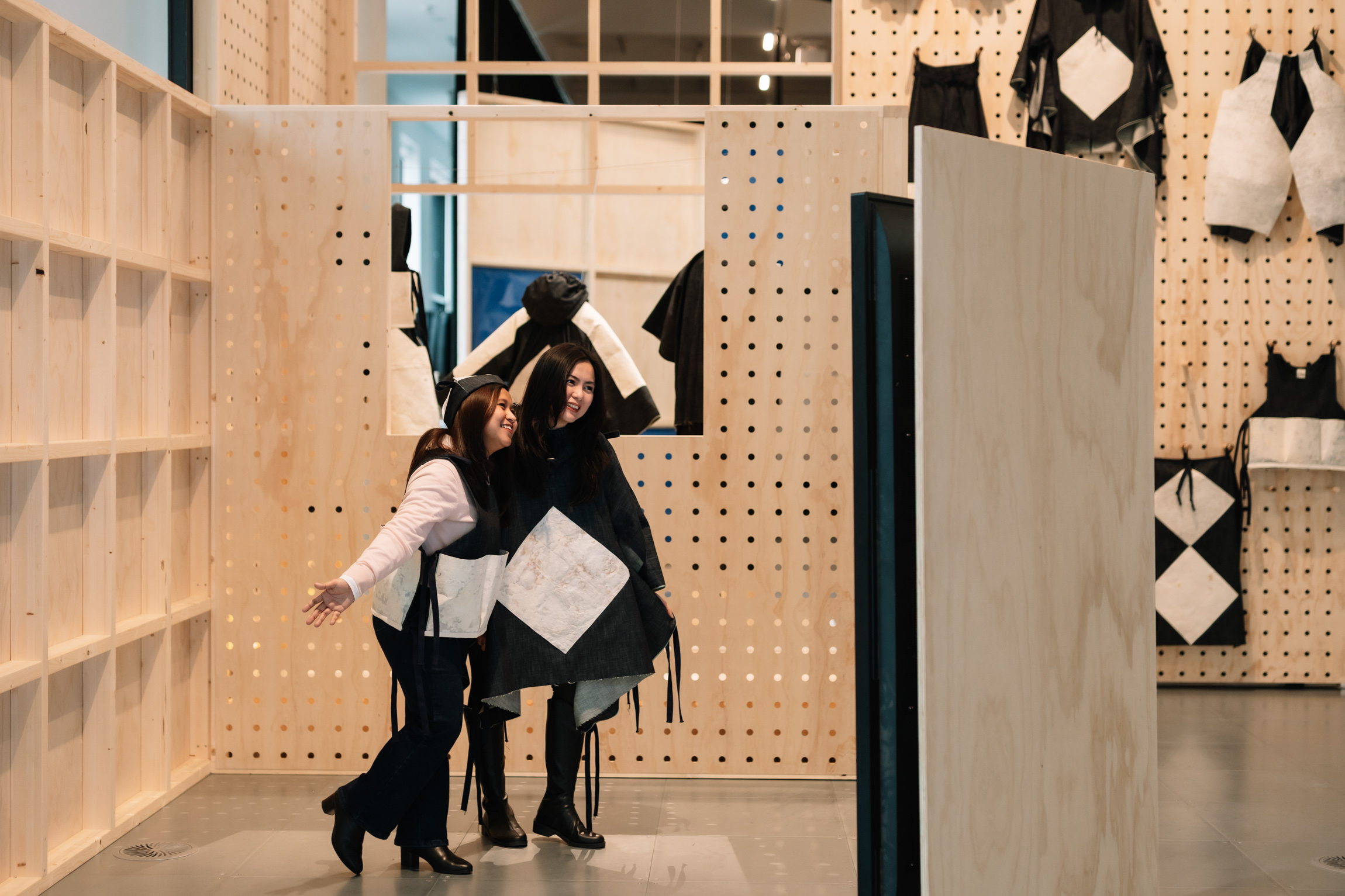 Two people wearing black and white designer clothing stand in a plywood display
