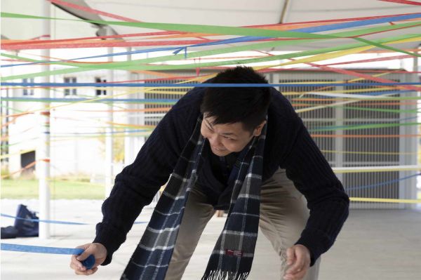 A man bends over to unroll a thread of coloured streamer