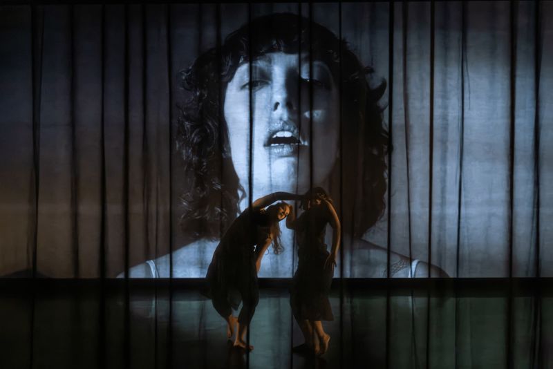 A dancer with arms in air with a projection of woman in background