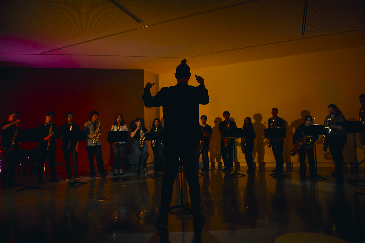 Concert curation a person conducts an orchestra standing in a dark gallery space