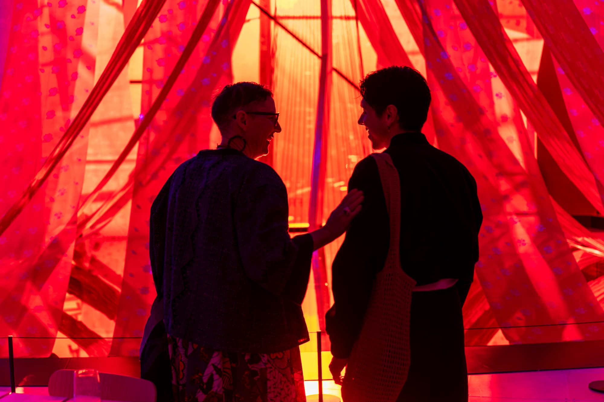 two people stand in front of a red robed installation talking
