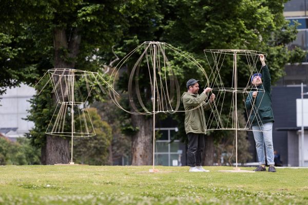 A kinetic sculpture moves in the foreground on the grass