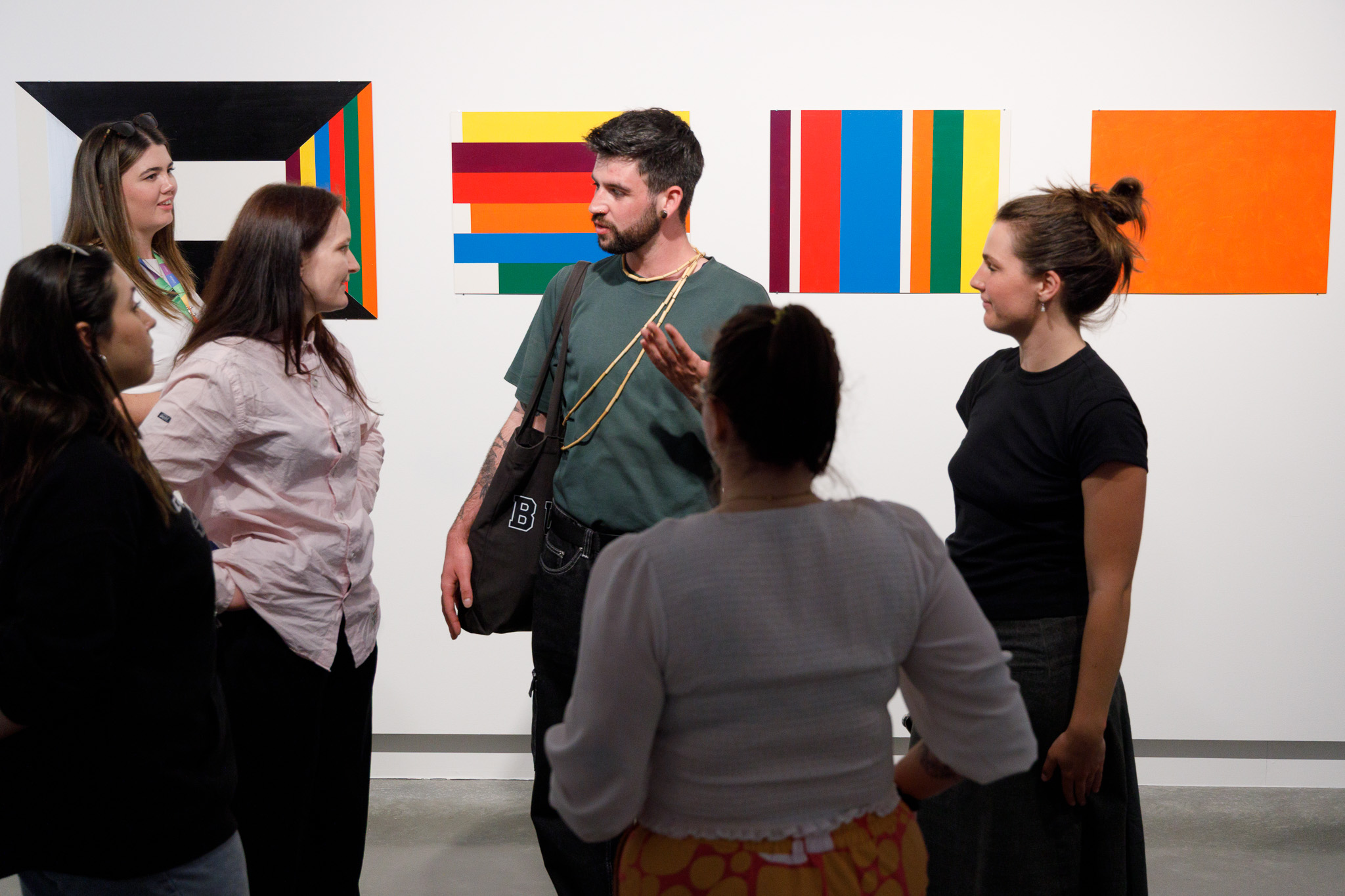 a group of students talk in a gallery in front of colourful artworks