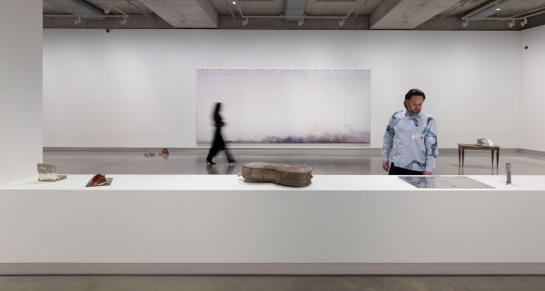 Two people walk in a white walled gallery with small sculptures on a walled plinth