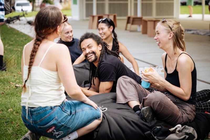A group of young people sit on a lawn in a garden and chat happily