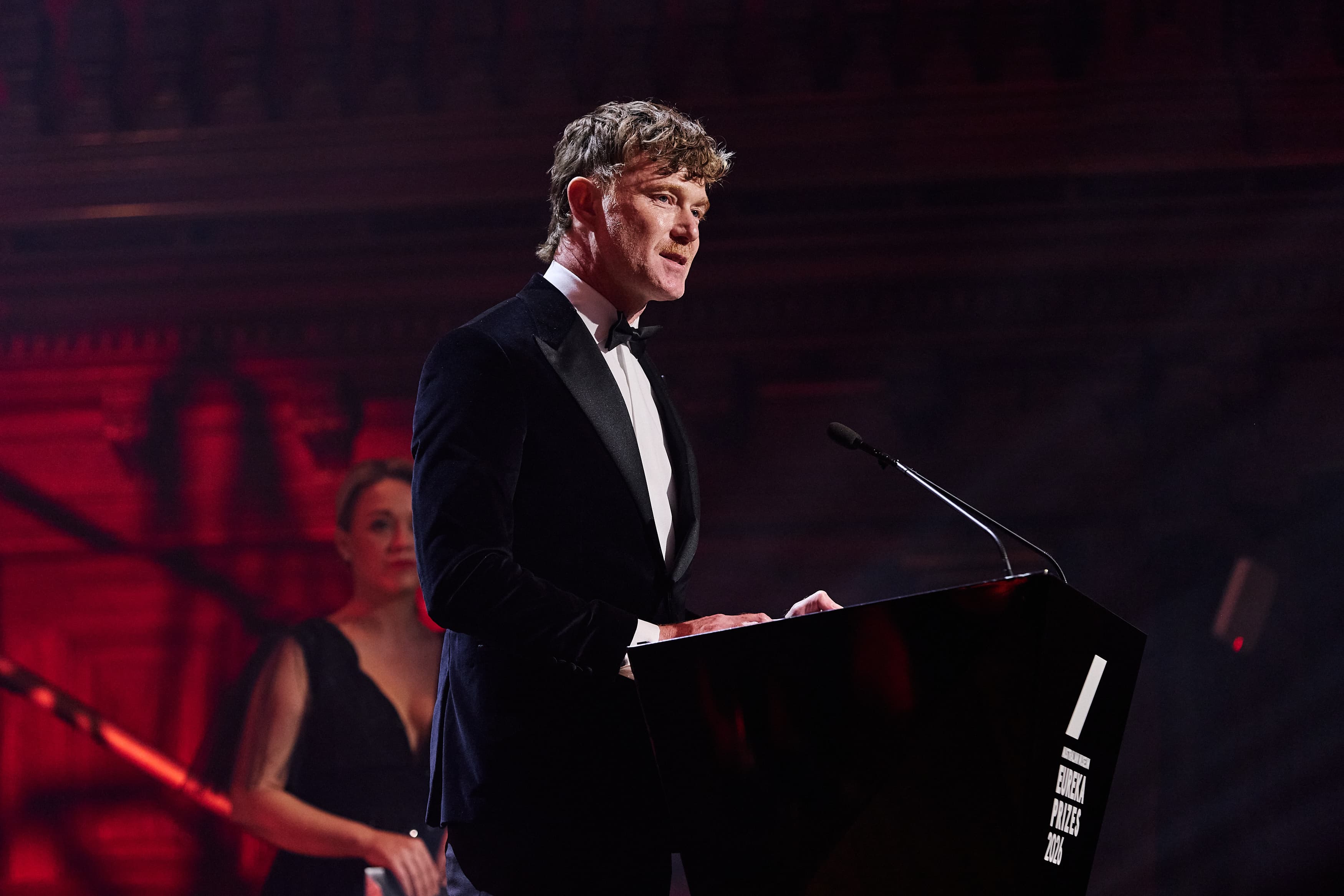 A person in black tie stands at a lectern on a stage