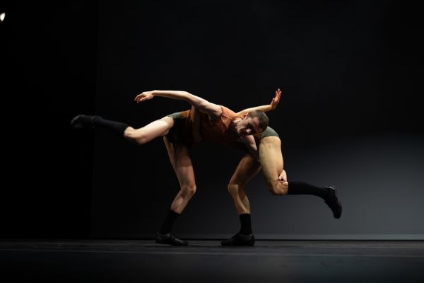 Two dancers entwined with legs and arms in air on dark stage