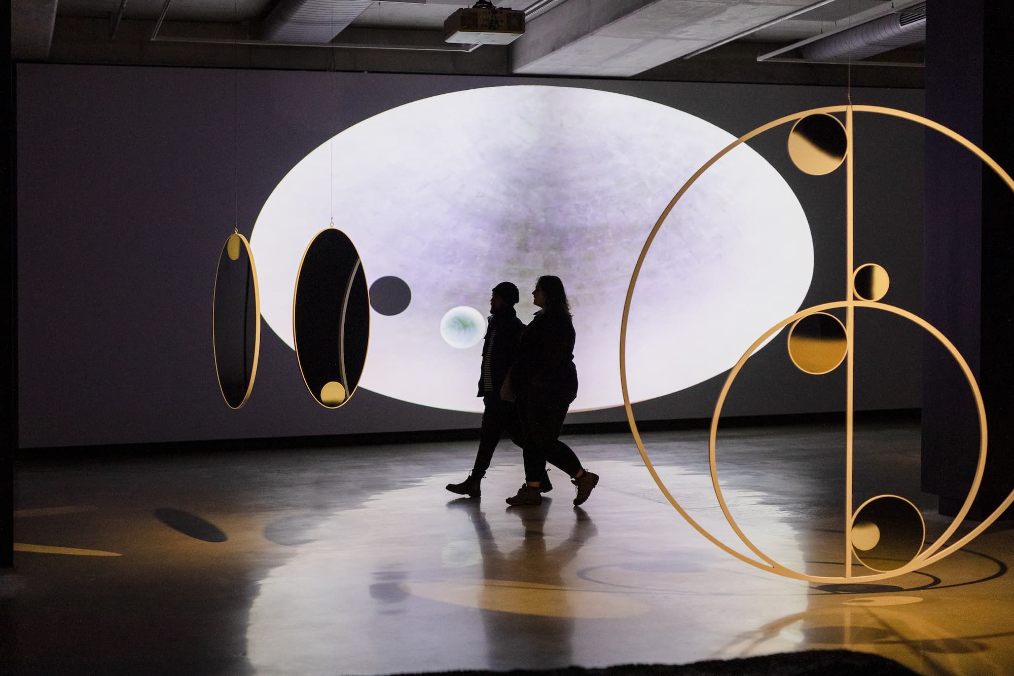 two people walk across a dark gallery