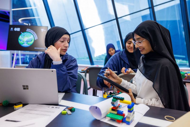 Three students in a classroom environment talk over lego