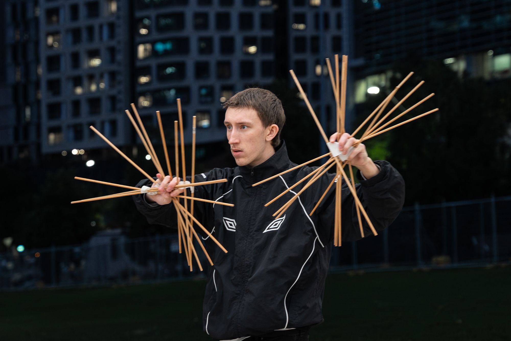 A person holding wooden sticks sprayed out in each finger on a dark city background