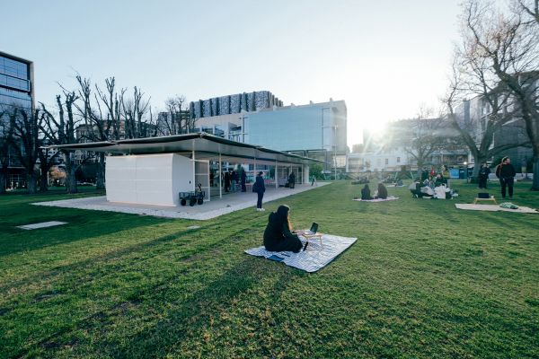 Student eat a picnic on the grass as the sun sets behind mpavilion