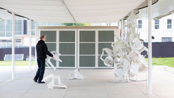 A person adds a plastic chair to a sculpture of plastic chairs
