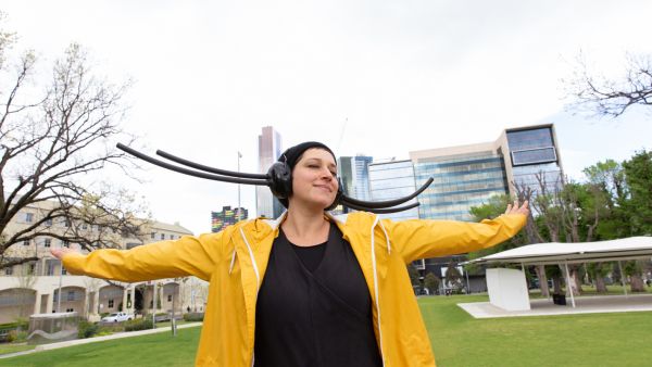 A woman in a yellow raincoat performs with headphones