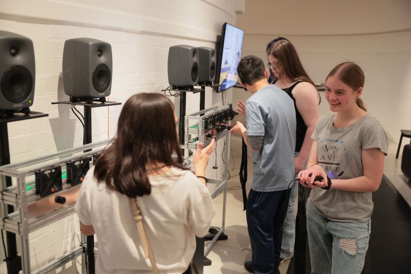 A person stands holding a haptic mouse with computers around them