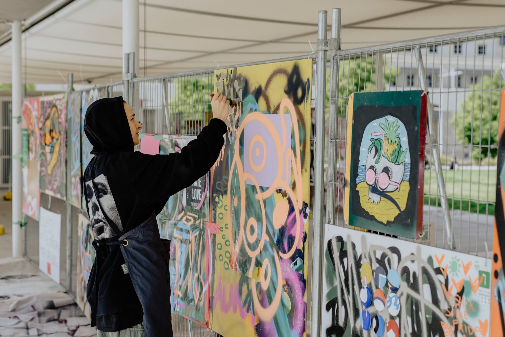 A person paints on a grafittied paper hanging from a mesh wall