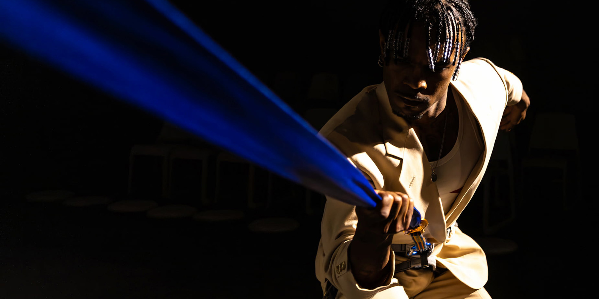 A person holds a blue ribbon and is in a performative stance