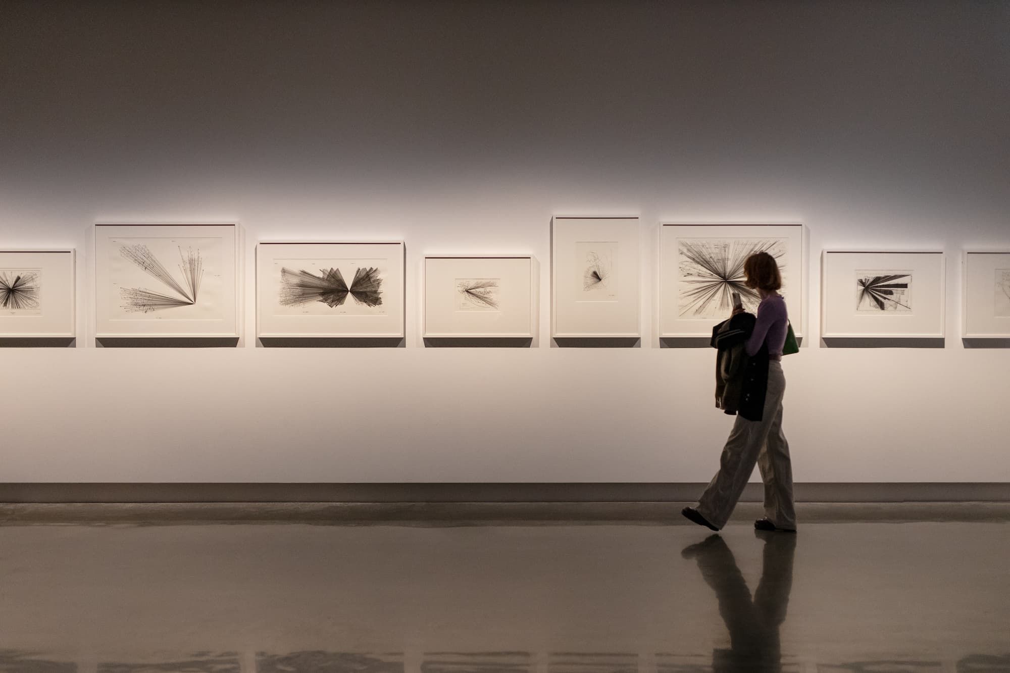 A woman walks past paintings in a gallery