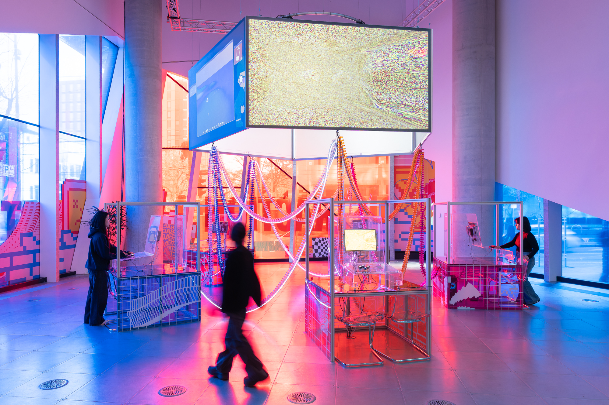 A brightly lit circular sculpture of screens and cables with people walking around computer consoles 