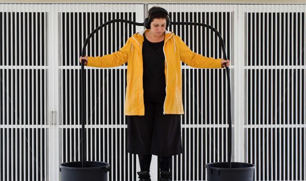 A woman stands with two pipes draping from her ears