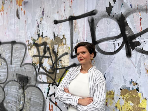 Sabina Andron stands cross-armed with graffiti in the background
